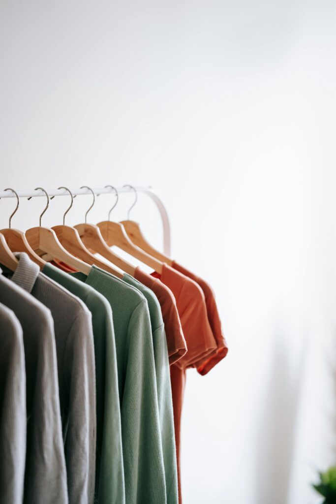 Light room interior with collection of various garments on wooden racks in wardrobe near white walls